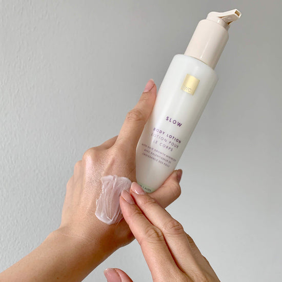 Hand holding a bottle of EW Slow Aloe Body Lotion with a gray background