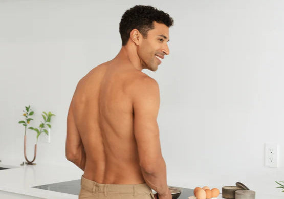 Shirtless man standing at kitchen stove
