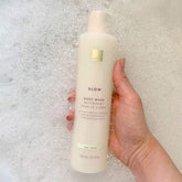 Hand holding a bottle of EWC Slow Aloe Body Wash against a bubble bath background