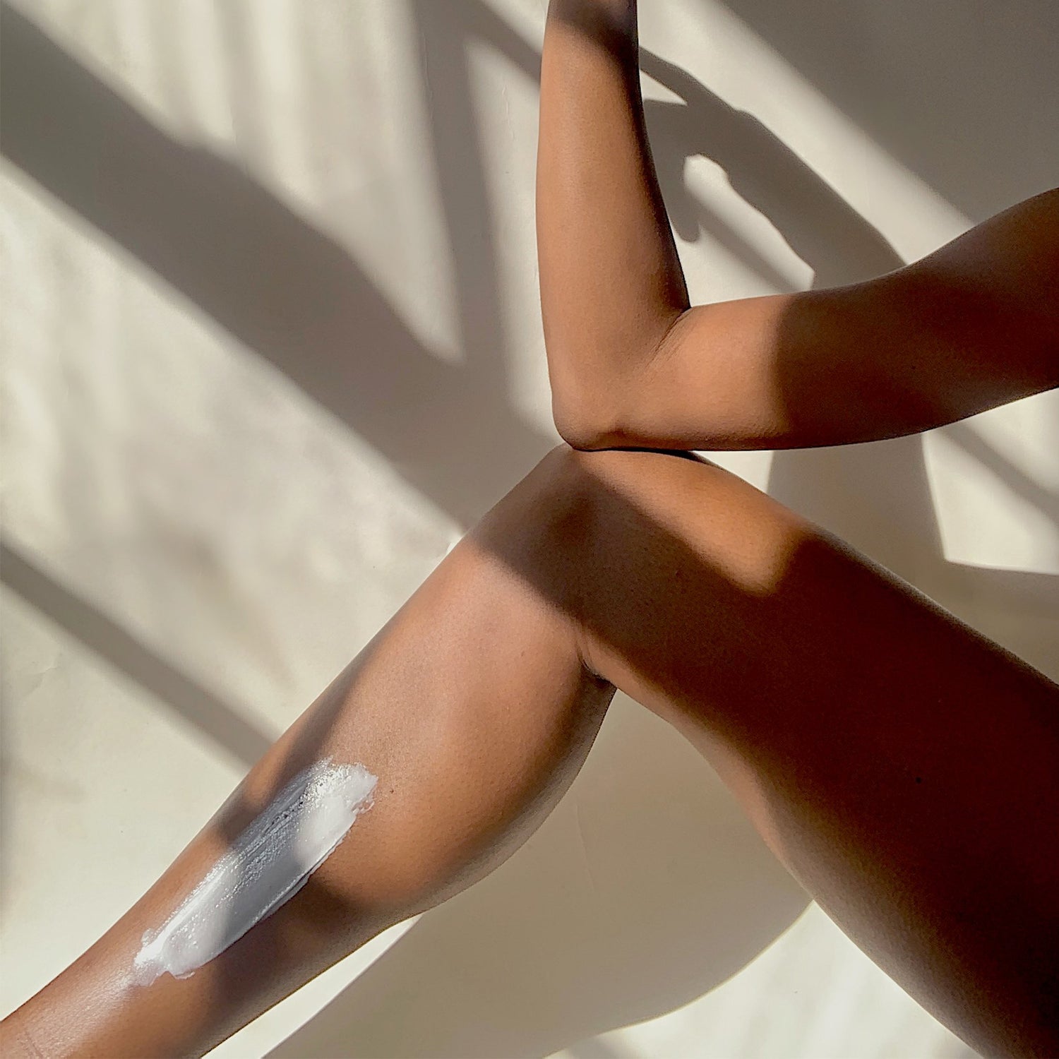 Person applying EWC Slow Shea Body Butter to their leg, against a neutral background