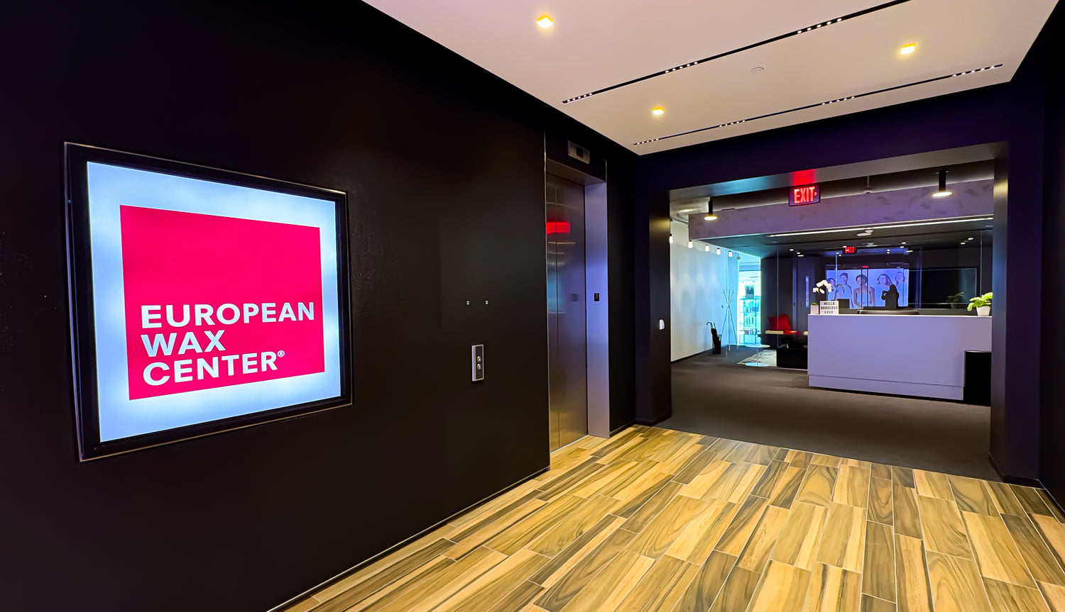 Entrance Lobby of the European Wax Center Corporate Office. There is a large EWC logo on the wall next to the elevators, and a reception desk.