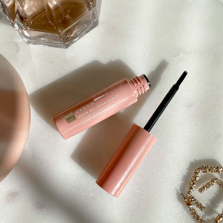 EWC GROOM Brow Building Serum open bottle and applicator on a marble dresser.