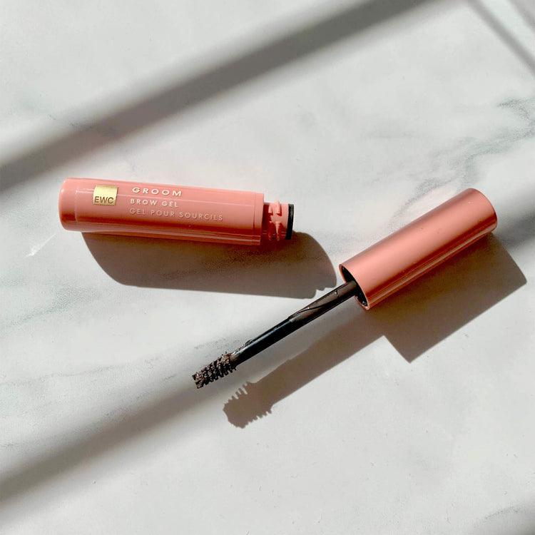 An open container of EWC GROOM Tinted Brow Gel resting on a marble table.