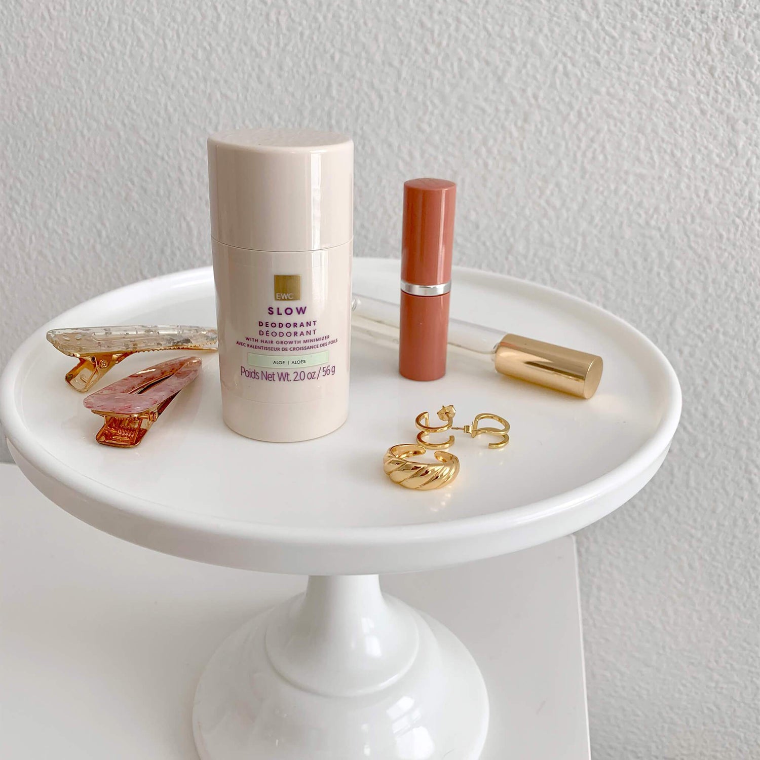 White round stand with EWC SLOW Aloe Deodorant stick, makeup, hair clips, and gold jewelry.