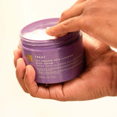 Hands holding an open tub of EWC TREAT Get Smooth Skin Clearing Body Cream.